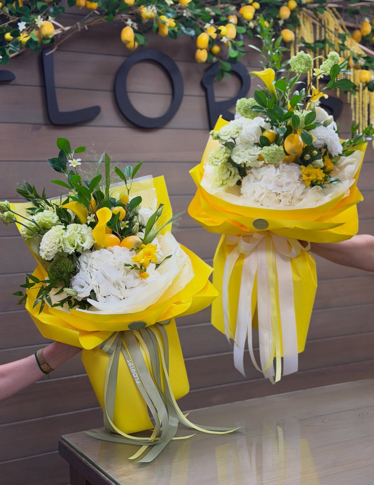 Two bouquets of white and yellow flowers wrapped in bright yellow paper.
